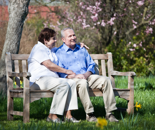 a senior and a loved one sitting on a bench on a warm sunny day