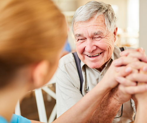 an older senior man smiling, holding hands with a caregiver