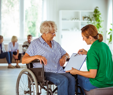 A person in a wheelchair is shown a document by another person wearing a green shirt.